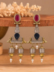 Pair of oxidised dual-tone jhumka earrings displayed upright on a wooden prop showing crimson, navy and amber stones with pearl drops