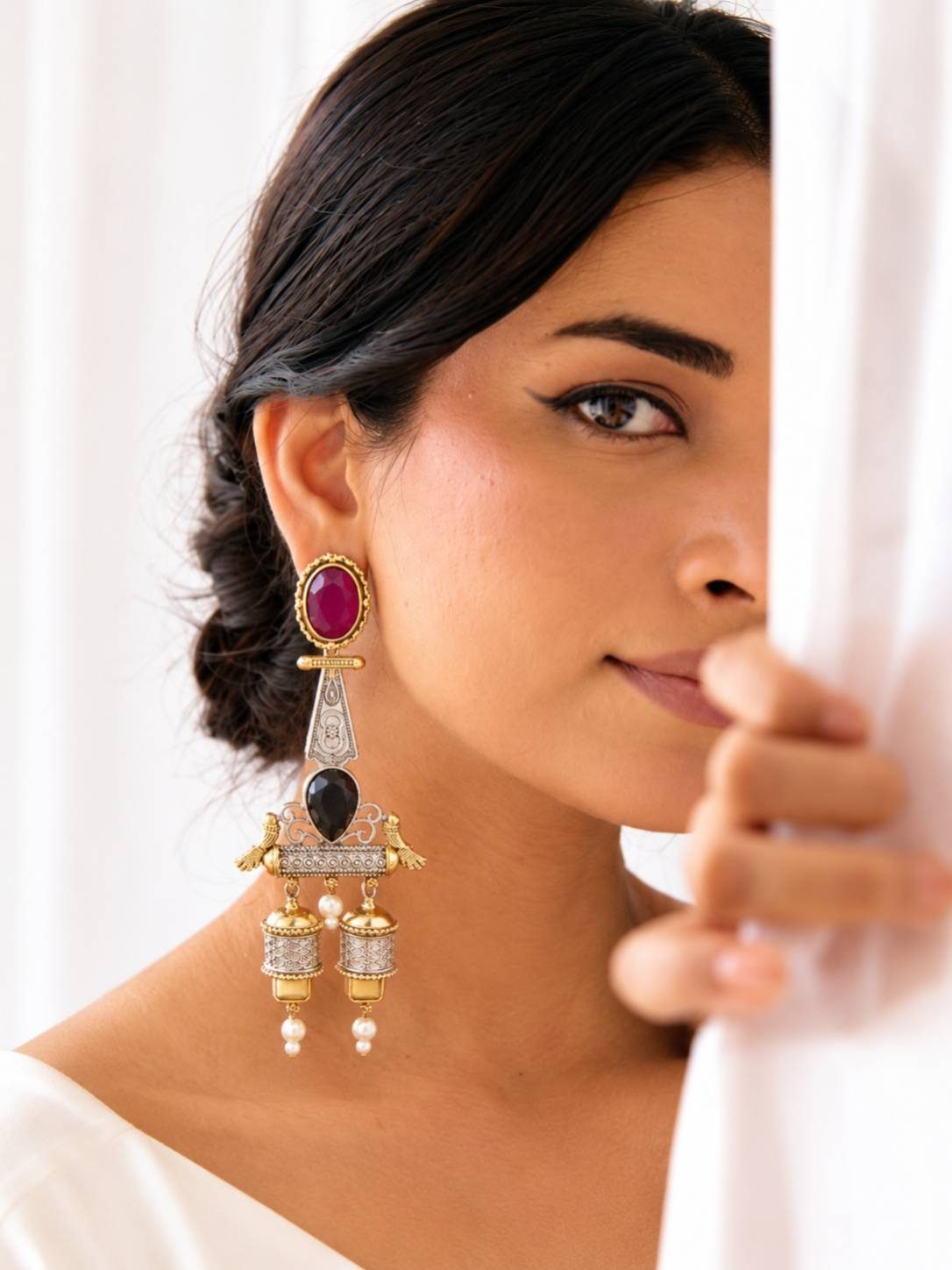 Woman wearing one large oxidised dual-tone jhumka earring against a white draped background showing earring scale and drape