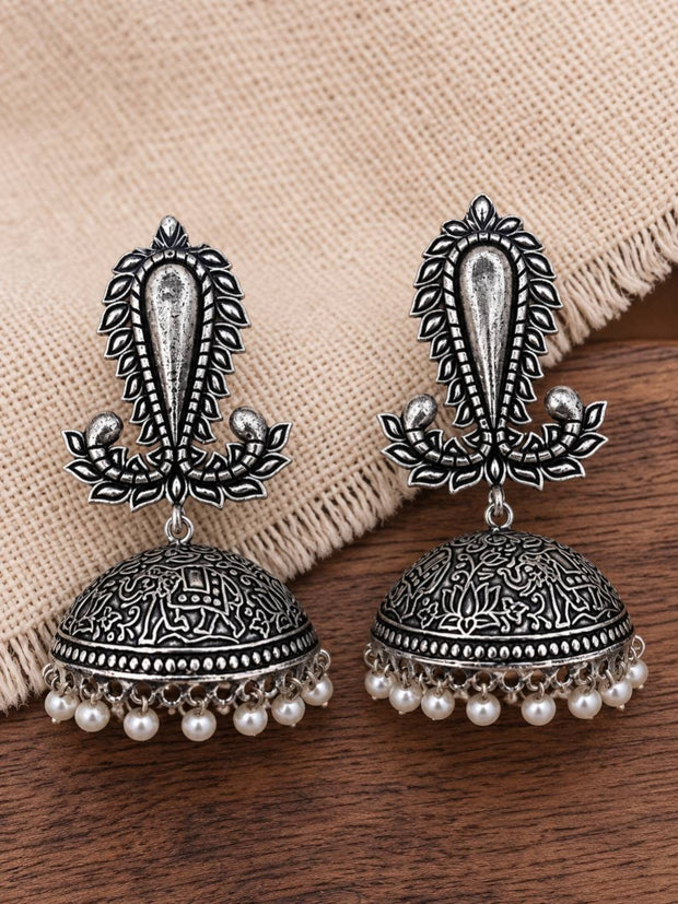Pair of oxidised silver jhumka earrings with engraved dome and white pearl drops laid on beige fabric