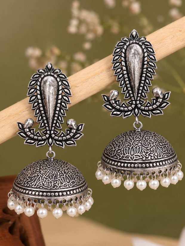 Oxidised silver paisley-top jhumka earrings with pearl fringe displayed on a wooden rod against green background
