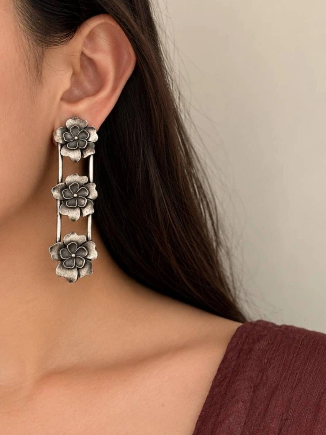 Oxidised silver three-flower drop earring worn on a woman's ear against a neutral background