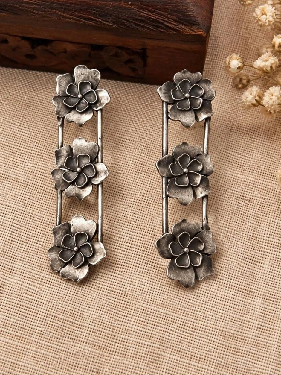 Two oxidised silver flower drop earrings laid flat on burlap beside a carved wooden box