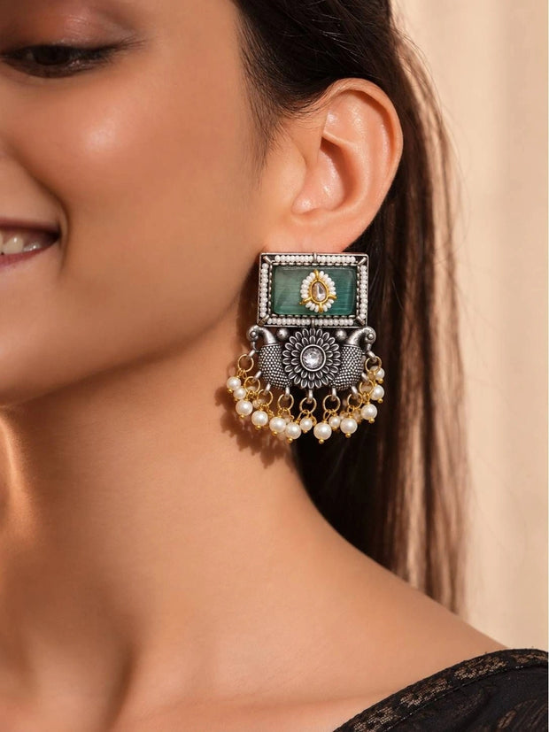 Woman wearing oxidised silver rectangular kundan earring with green stone and pearl fringe on right ear