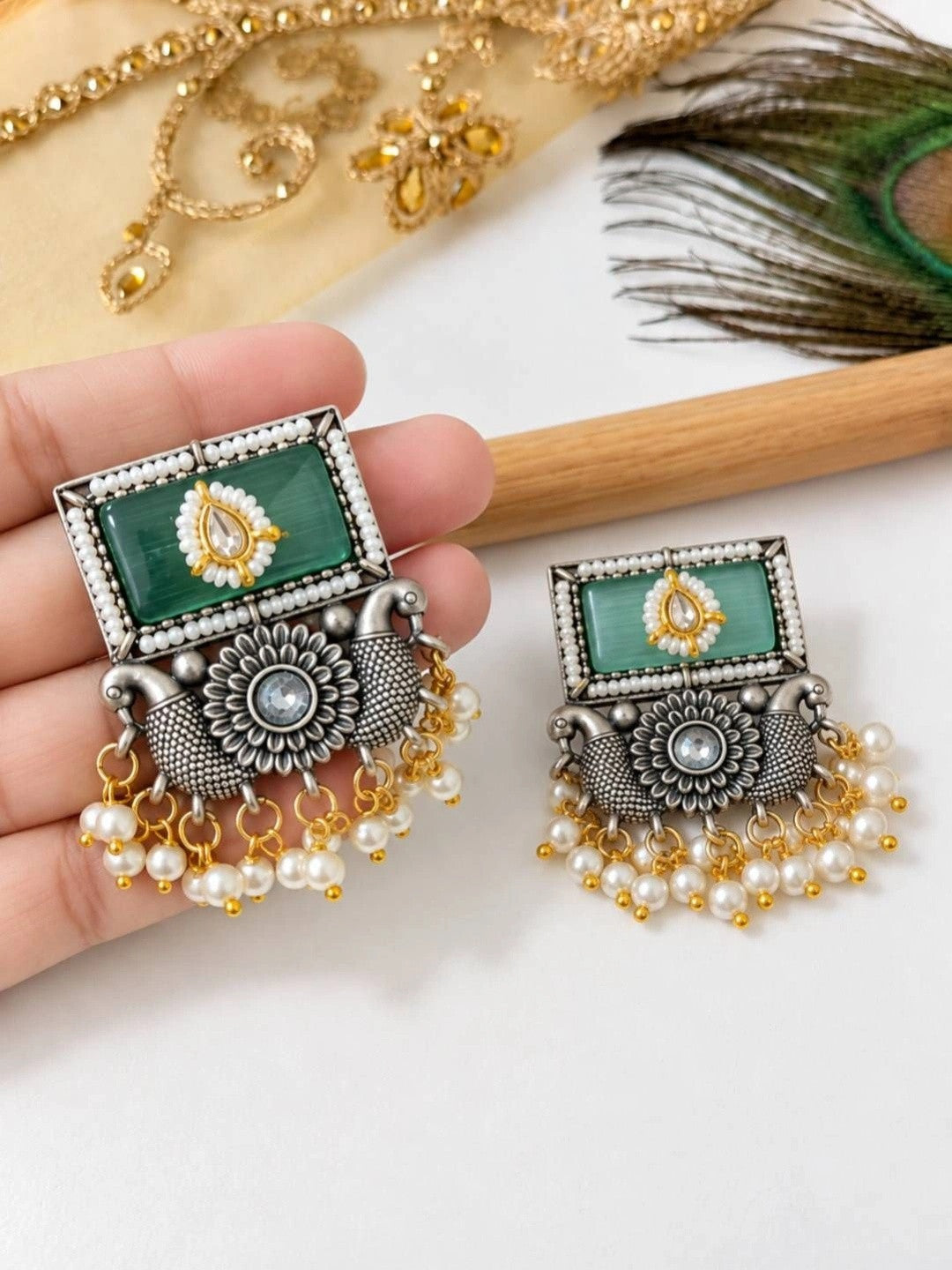 Front view of oxidised silver rectangular earring held in hand showing green stone and pearl drops alongside second earring