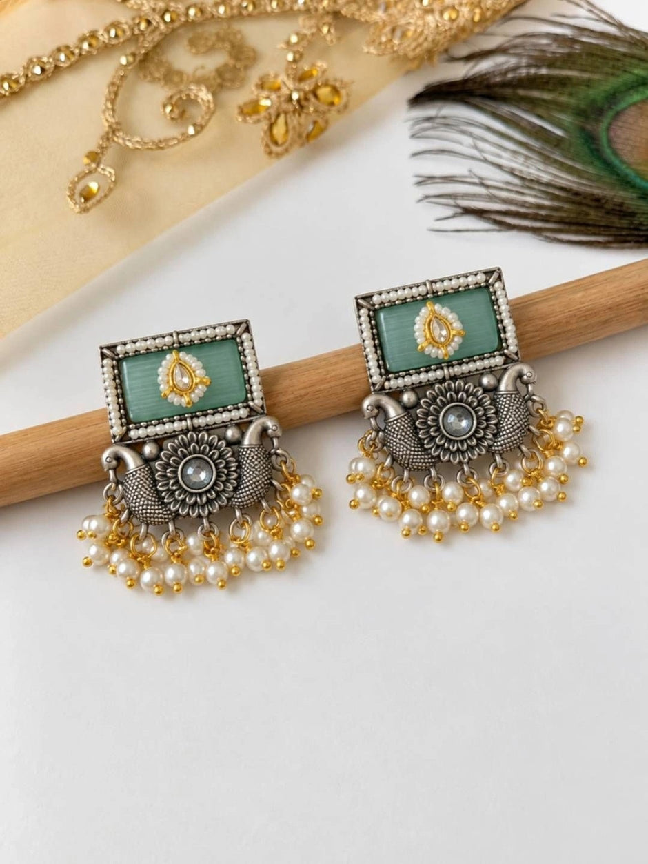 Pair of oxidised silver kundan rectangular drop earrings displayed on wooden rod with pearl fringe visible