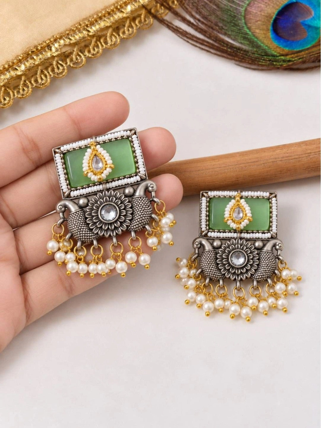 Pair of oxidised kundan square earrings with pearl drops held in hand showing front detail