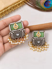 Pair of oxidised kundan square earrings with pearl drops held in hand showing front detail