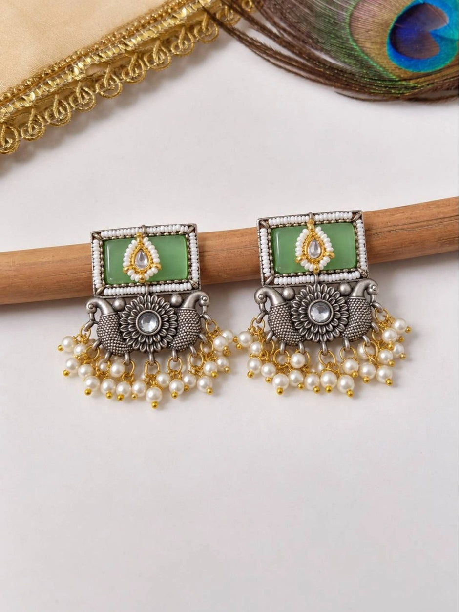 Both oxidised silver square kundan earrings with cascading ivory pearl dangles resting on wooden stick
