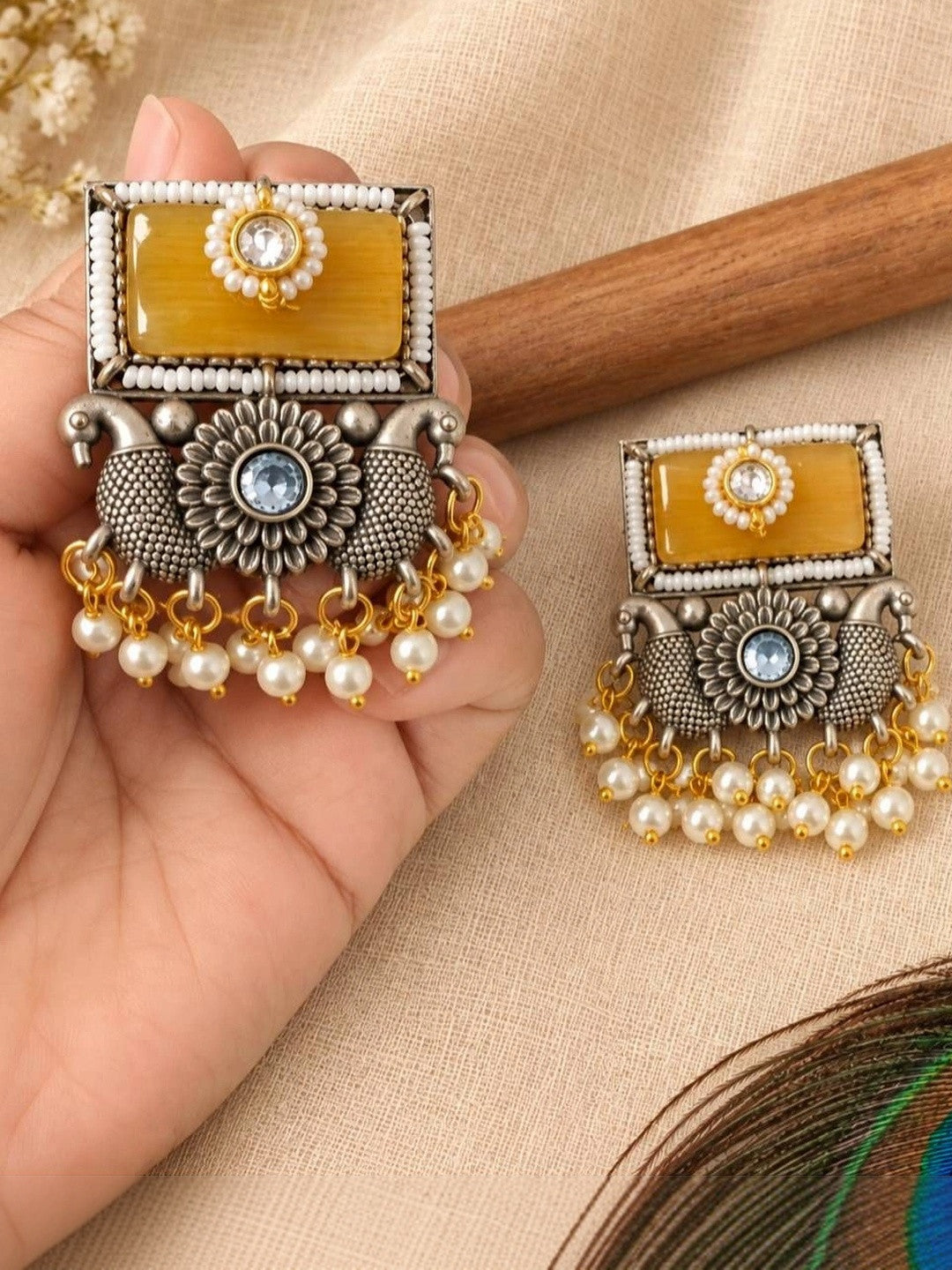 Pair of oxidised silver chandbali earrings held in hand showing peacock motif and pearl bead fringe