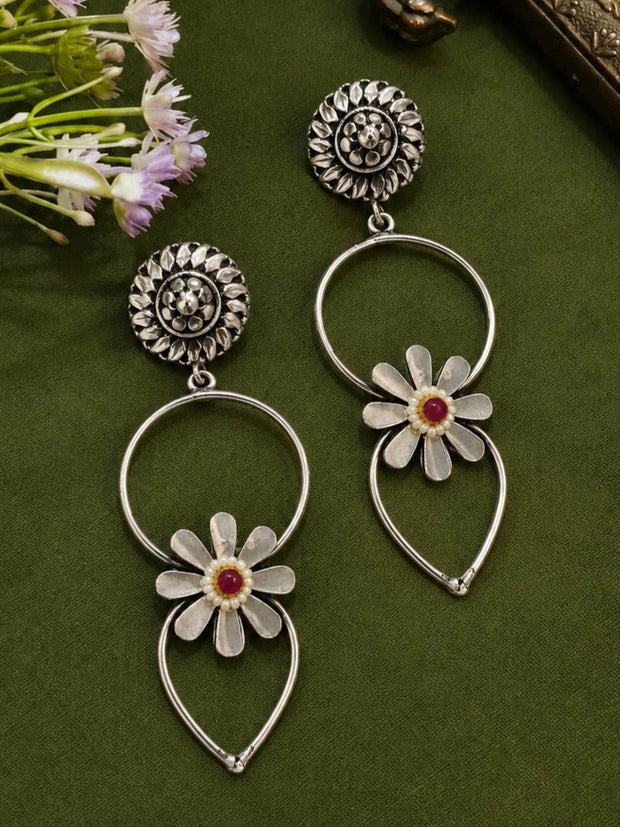 Front view of both oxidised silver daisy hoop drop earrings on green fabric with purple flowers
