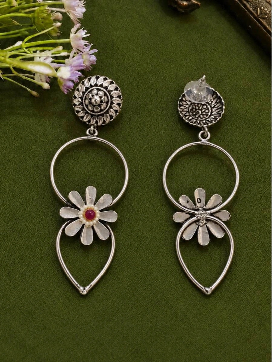 Back view of oxidised silver daisy hoop earrings showing push-back stud post on green fabric