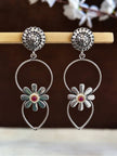 Pair of oxidised silver daisy hoop drop earrings displayed upright on a wooden prop against brown background