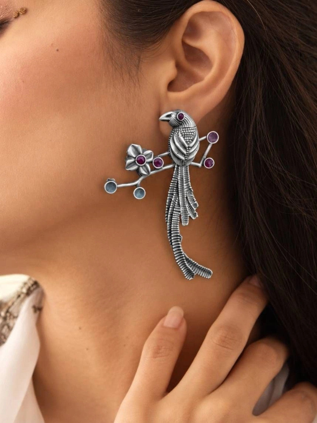 Woman wearing oxidised silver long-tailed bird drop earring with pink stone embellishments on ear