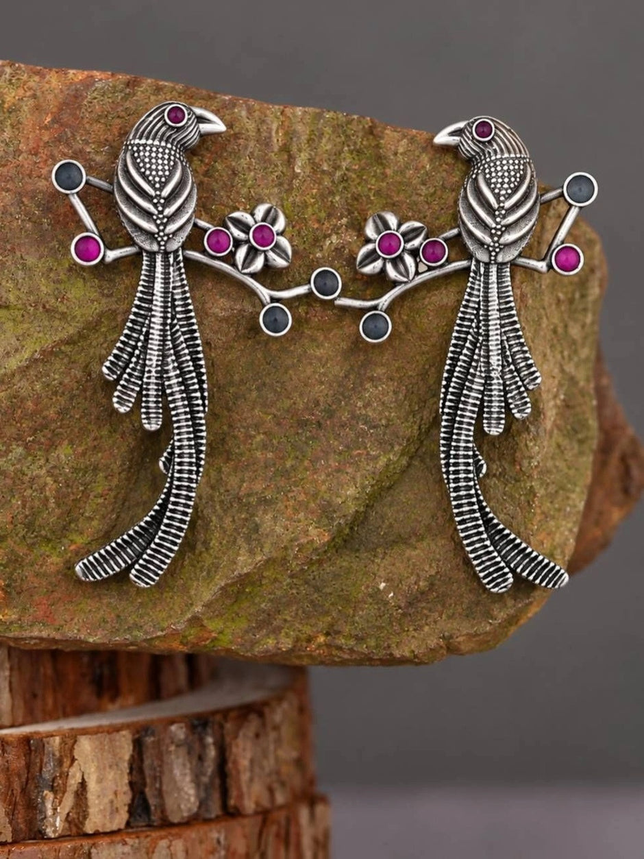 Both oxidised silver bird branch drop earrings displayed side by side on a textured stone surface