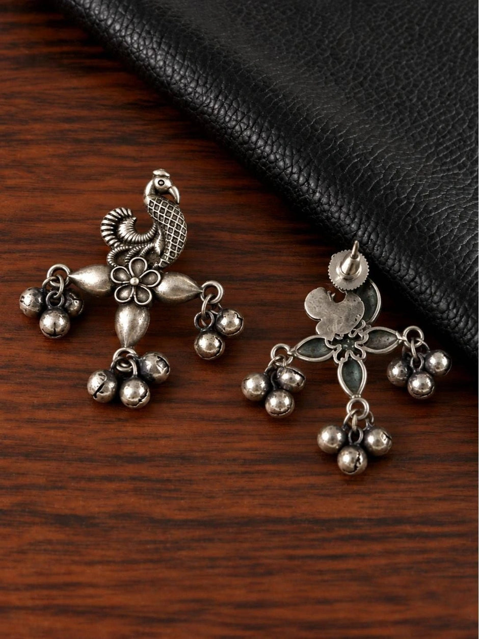 Front and back view of oxidised silver peacock earrings on a wooden surface