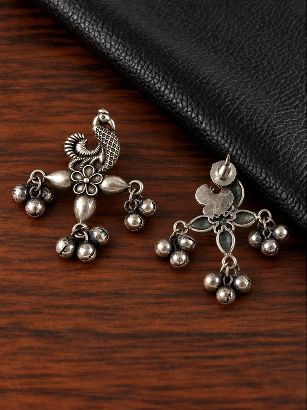 Front and back view of oxidised silver peacock earrings on a wooden surface
