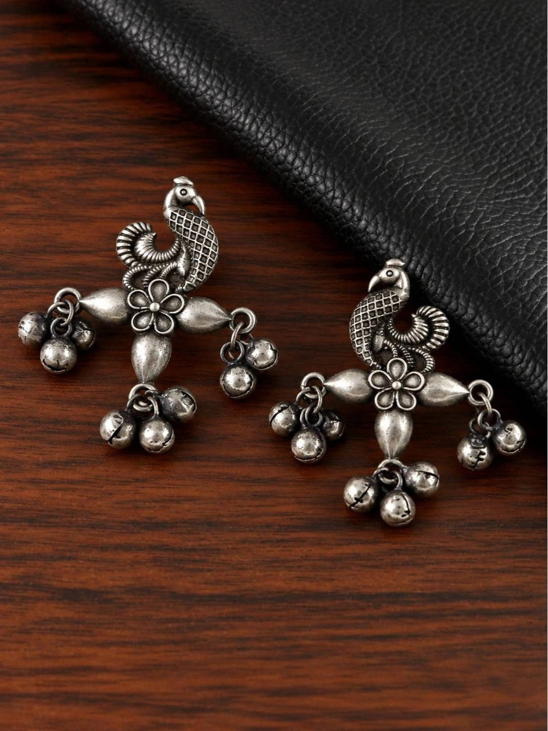 Pair of oxidised silver peacock drop earrings with ghungroo bells on wood
