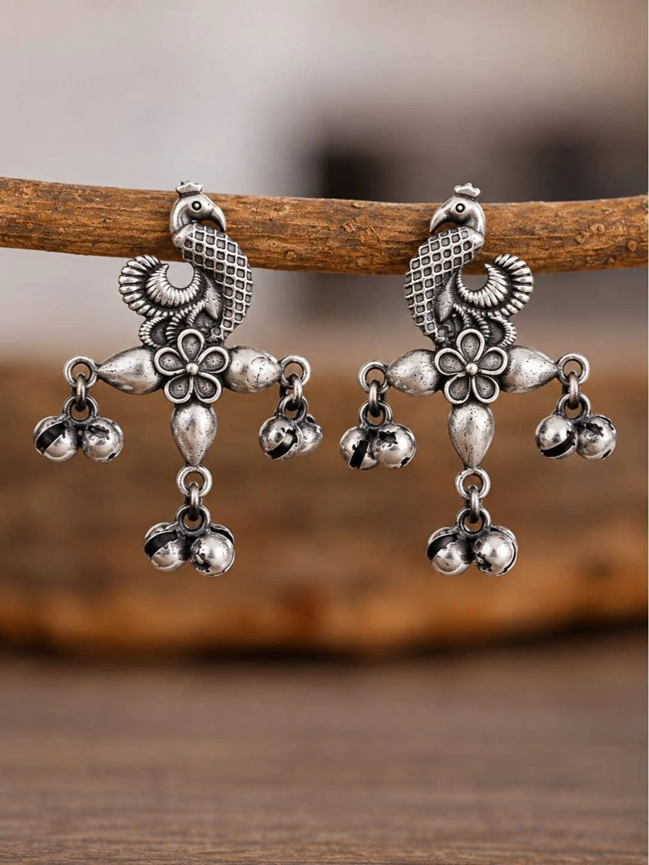Close-up of two oxidised silver peacock earrings hanging from a wooden branch