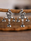 Close-up of two oxidised silver peacock earrings hanging from a wooden branch