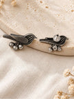 Pair of oxidised silver bird stud earrings with ghungroo bells laid flat on a stone surface, reverse side visible on one earring