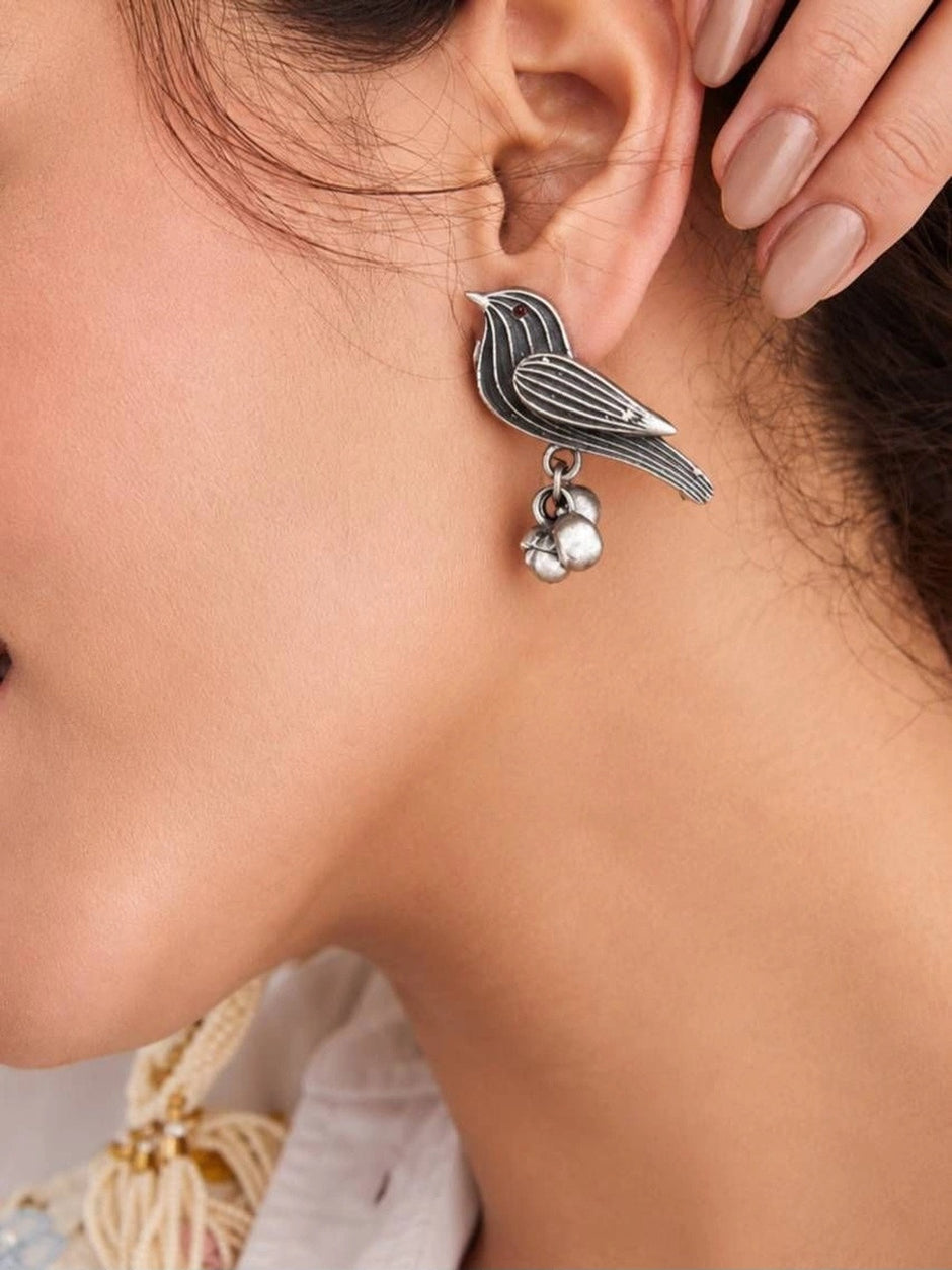 Close-up of oxidised silver bird stud earring with ghungroo cluster worn on a woman's ear