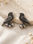 Pair of oxidised silver bird earrings with ghungroo drops resting against a textured stone prop, front view