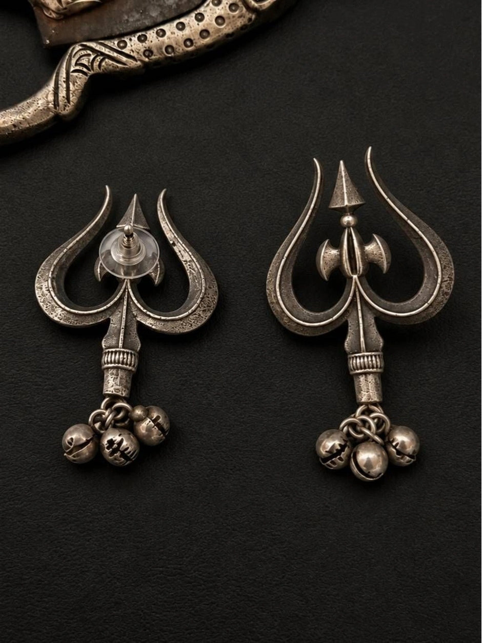 Front and back view of oxidised silver trishul stud earrings with ghungroo bell drops on dark background