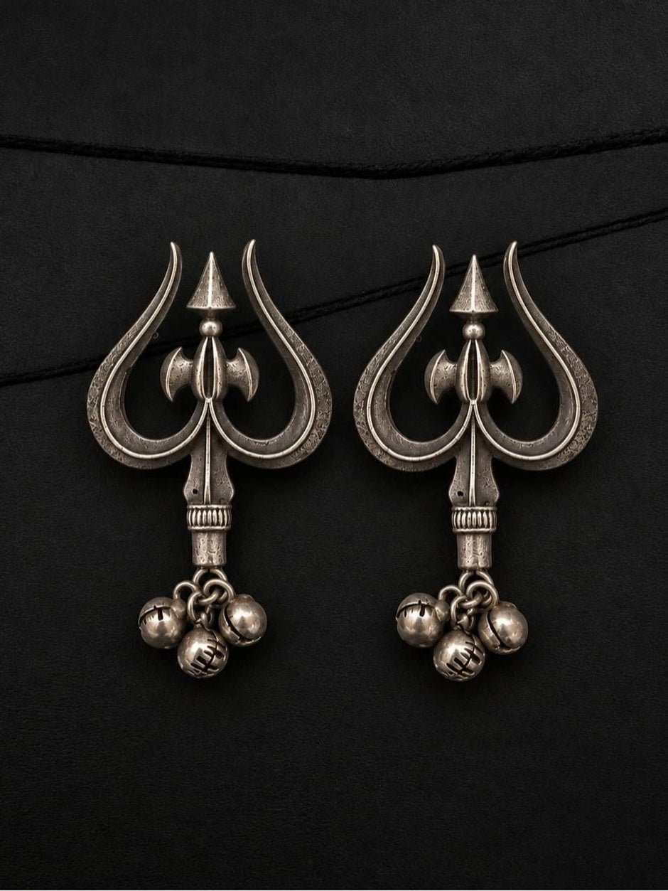 Pair of oxidised silver trishul drop earrings with parsu motif and three ghungroo bells laid flat on black surface