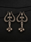 Pair of oxidised silver trishul drop earrings with parsu motif and three ghungroo bells laid flat on black surface