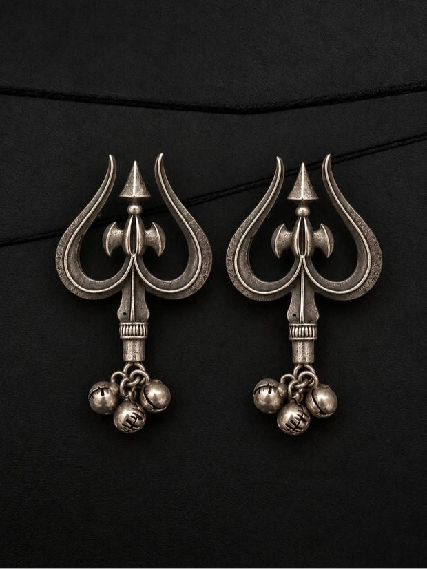 Pair of oxidised silver trishul drop earrings with parsu motif and three ghungroo bells laid flat on black surface