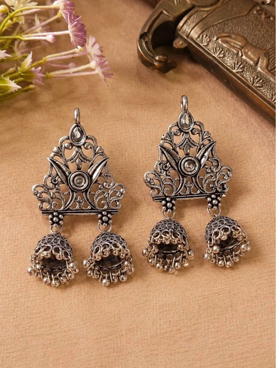Front view of both oxidised silver double jhumka earrings laid flat on beige fabric with purple flowers