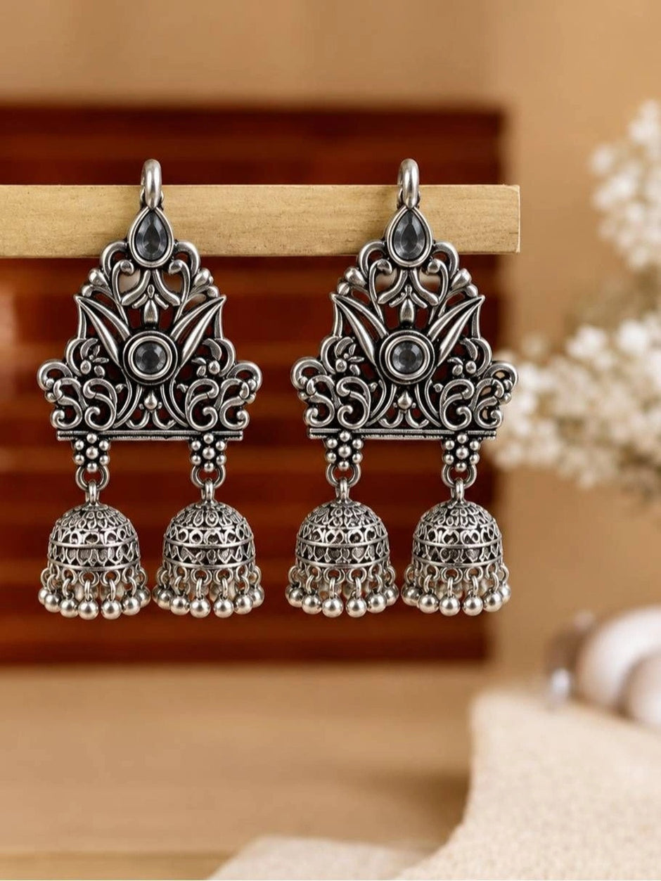 Pair of oxidised silver double jhumka earrings hanging on a wooden display bar against soft background