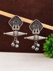 Pair of oxidised silver coin drop earrings with ghungroo bells hanging on a wooden rod against a dark background