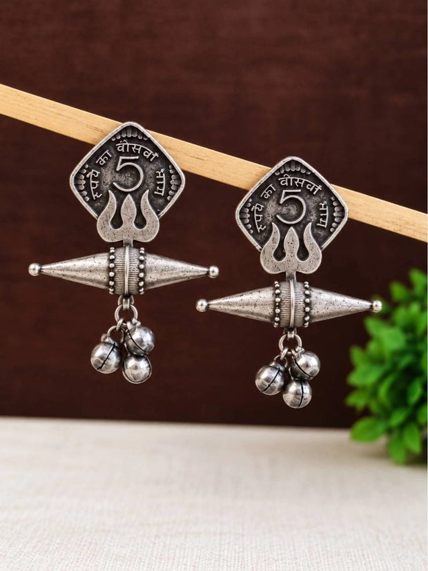 Pair of oxidised silver coin drop earrings with ghungroo bells hanging on a wooden rod against a dark background