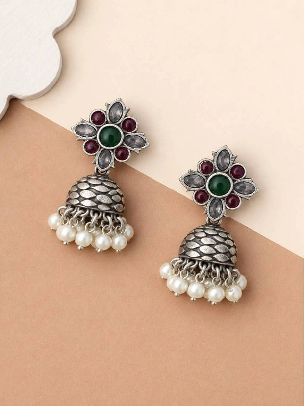 Pair of oxidised silver floral kundan jhumka earrings laid flat on a beige surface
