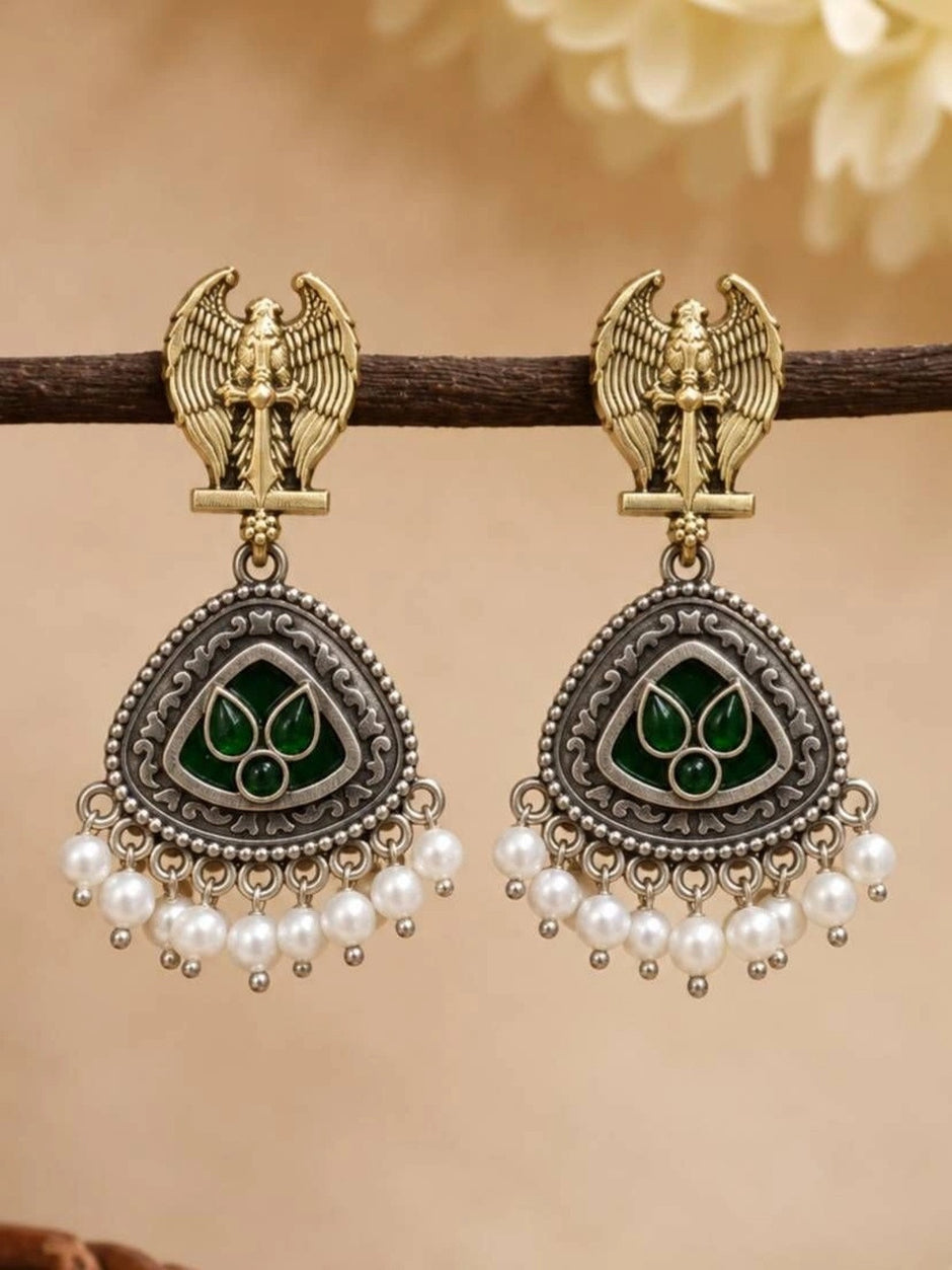 Oxidised Garuda chandbali earrings with pearl drops hanging from a wooden branch against warm background