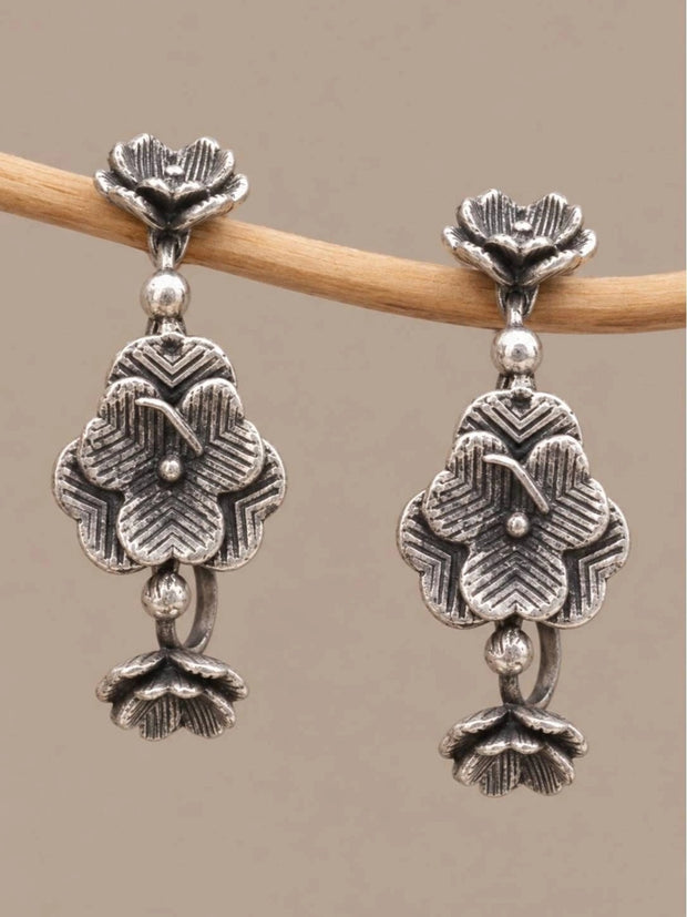 Pair of oxidised silver floral ear cuff earrings with layered petal motifs hanging on a wooden branch