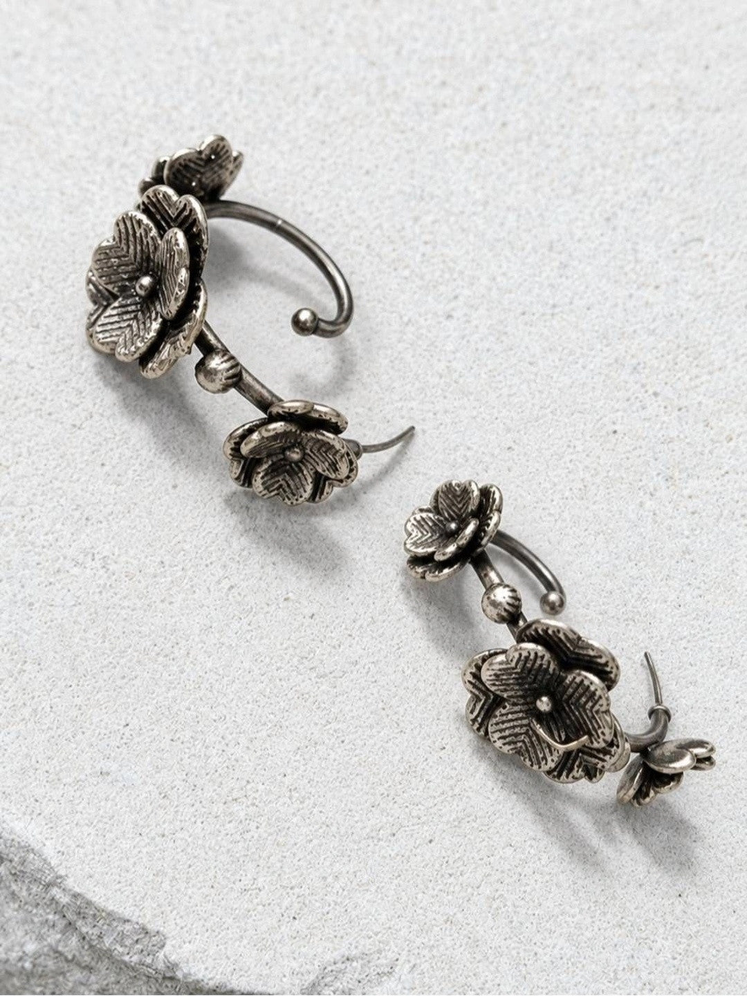 Two oxidised silver floral ear cuff earrings laid flat on a white stone surface showing the stud posts