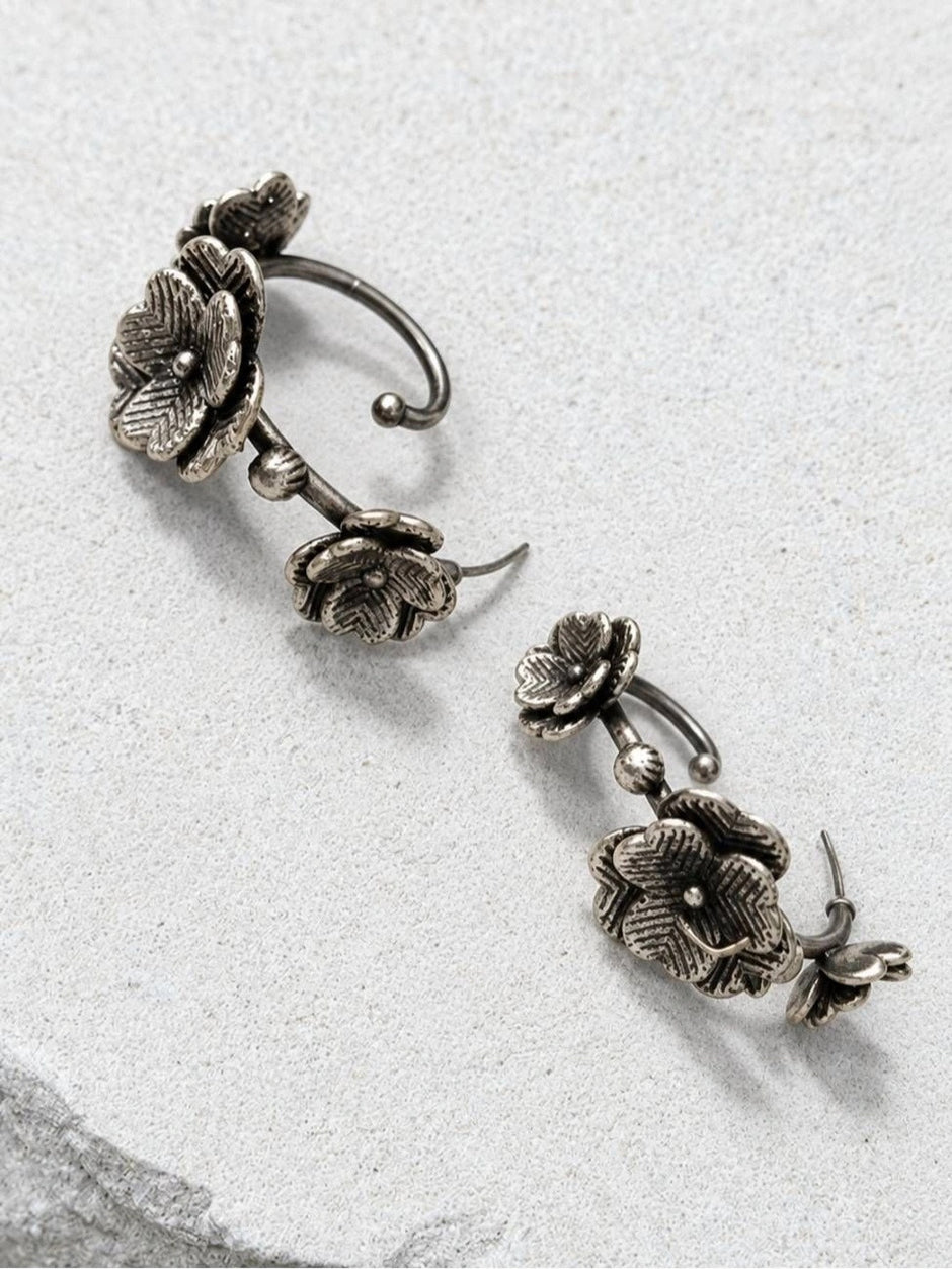 Two oxidised silver floral ear cuff earrings laid flat on a white stone surface showing the stud posts