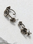 Two oxidised silver floral ear cuff earrings laid flat on a white stone surface showing the stud posts