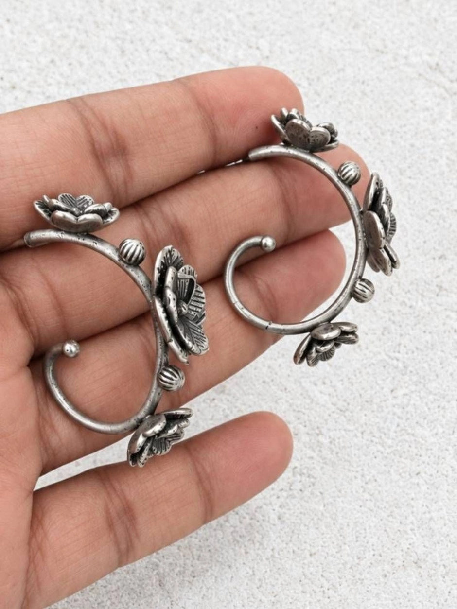 Both oxidised silver floral ear cuff earrings held in an open palm showing the curved stem and petal details