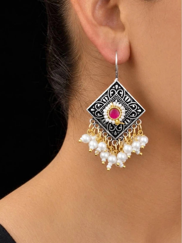 Oxidised silver diamond-shaped drop earring with magenta stone and pearl clusters worn on ear