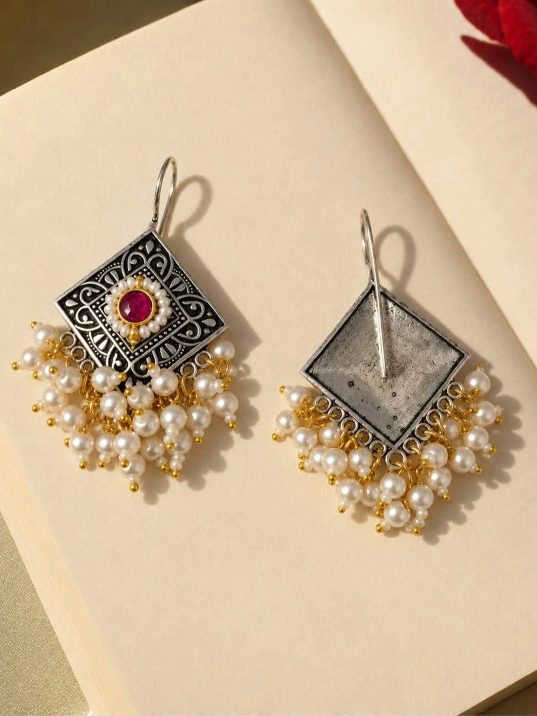 Front and back view of oxidised silver pearl drop earrings laid flat on cream surface
