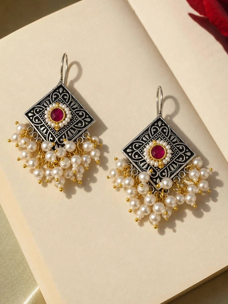 Pair of oxidised silver earrings with engraved scroll motifs and white pearl clusters on cream background