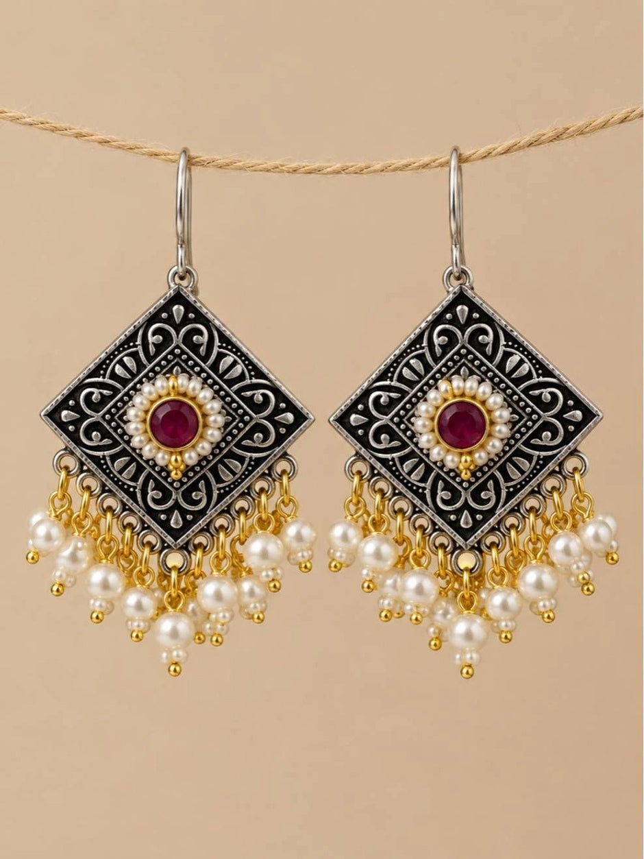 Pair of oxidised silver diamond-shaped earrings with pearl drops hanging from rope against beige background