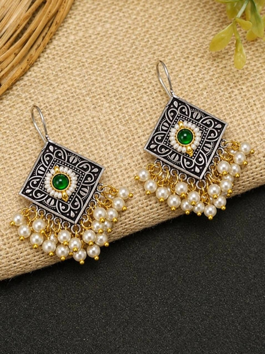 Pair of oxidised silver diamond earrings with green cabochon and pearl fringe displayed on jute surface