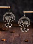Two oxidised silver elephant earrings with ghungroo balls hanging on a wooden display rod