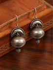 Close-up pair of oxidised silver dome jhumka earrings resting on carved wooden tray showing rope-edge detailing
