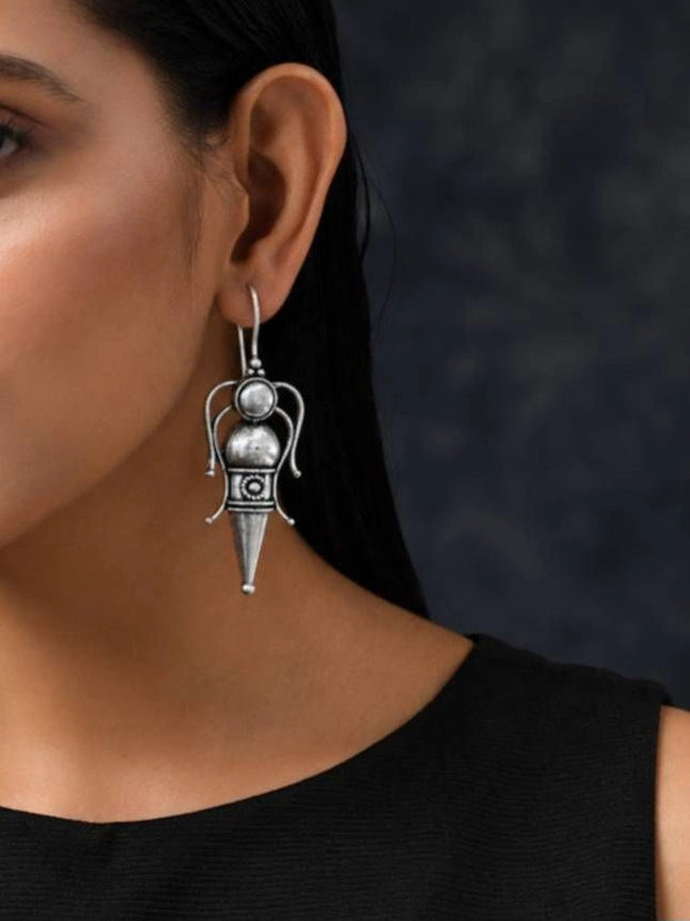 Woman wearing an oxidised silver goddess figure drop earring on shepherd hook wire against a dark background