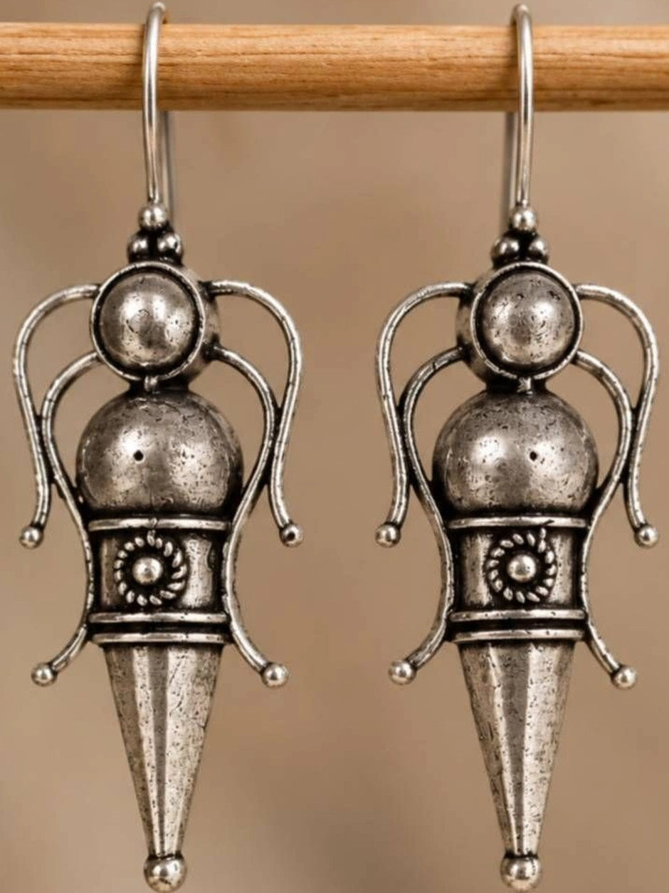 Close-up of two oxidised silver goddess drop earrings hanging on a wooden rod showing engraved medallion waist detail